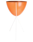 In front of a white background is an orange colored bullet planter. The planter has a wide top and narrows at the bottom. The planter is held up by a white metal stand. The stand has three white metal legs.