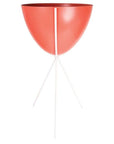 In front of a white background is a red colored bullet planter. The planter has a wide top and narrows at the bottom. The planter is held up by a white metal stand. The stand has three white metal legs.