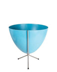 In front of white background is a bright blue planter in a short silver metal stand. The bullet planter is wide at the top and narrow at the bottom. The metal stand has three legs.