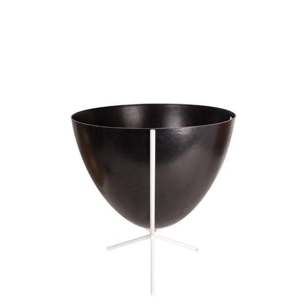 In front of white background is a black bullet planter in a short white metal stand. The bullet planter is wide at the top and narrow at the bottom. The metal stand has three legs. 