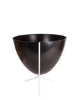 In front of white background is a black bullet planter in a short white metal stand. The bullet planter is wide at the top and narrow at the bottom. The metal stand has three legs.