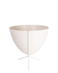 In front of white background is a white bullet planter in a short white metal stand. The bullet planter is wide at the top and narrow at the bottom. The metal stand has three legs.