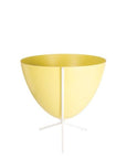 In front of white background is a yellow planter in a short white metal stand. The bullet planter is wide at the top and narrow at the bottom. The metal stand has three legs.