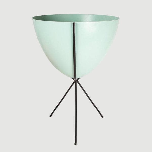 In front of white background is a turquoise planter in a black metal stand. The bullet planter is wide at the top and narrow at the bottom. The metal stand has three legs. 
