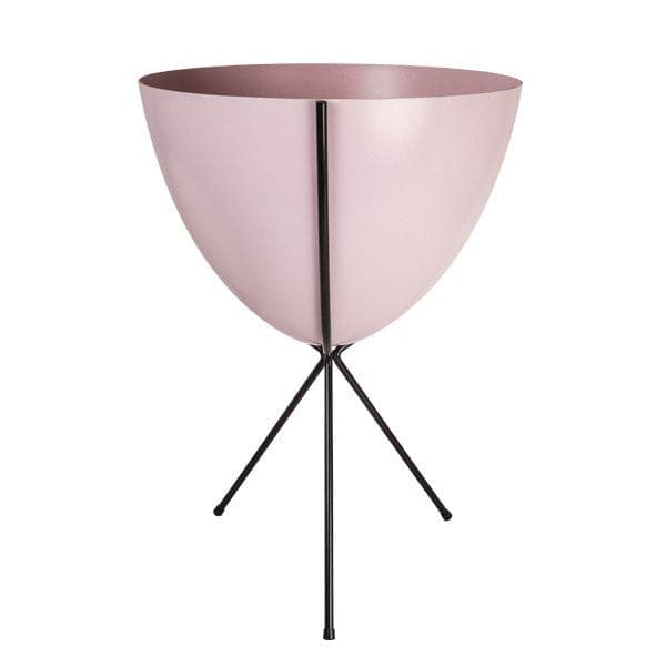 In front of white background is a soft pink planter in a black metal stand. The bullet planter is wide at the top and narrow at the bottom. The metal stand has three legs. 