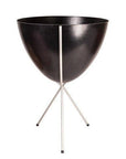 In front of white background is a black planter in a silver metal stand. The bullet planter is wide at the top and narrow at the bottom. The metal stand has three legs.