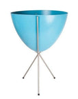 In front of white background is a bright blue planter in a silver metal stand. The bullet planter is wide at the top and narrow at the bottom. The metal stand has three legs.