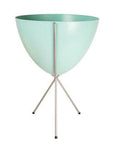 In front of white background is a turquoise planter in a silver metal stand. The bullet planter is wide at the top and narrow at the bottom. The metal stand has three legs.