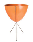 In front of white background is an orange planter in a silver metal stand. The bullet planter is wide at the top and narrow at the bottom. The metal stand has three legs.