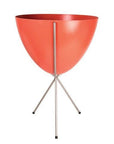 In front of white background is a red planter in a silver metal stand. The bullet planter is wide at the top and narrow at the bottom. The metal stand has three legs.