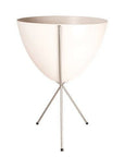 In front of white background is a white planter in a silver metal stand. The bullet planter is wide at the top and narrow at the bottom. The metal stand has three legs.