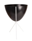 In front of white background is a black planter in a white metal stand. The bullet planter is wide at the top and narrow at the bottom. The metal stand has three legs.