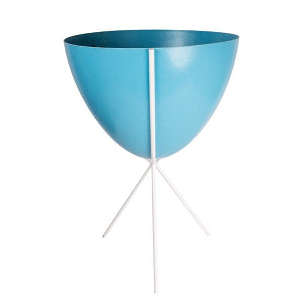In front of white background is a bright blue planter in a white metal stand. The bullet planter is wide at the top and narrow at the bottom. The metal stand has three legs. 