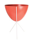In front of white background is a red planter in a white metal stand. The bullet planter is wide at the top and narrow at the bottom. The metal stand has three legs.