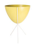 In front of white background is a yellow planter in a white metal stand. The bullet planter is wide at the top and narrow at the bottom. The metal stand has three legs.