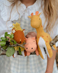 A stuffed animal set inspired by the Savannah. It includes a pink hippo, a red lion with a yellow mane, and a mustard yellow giraffe with orange spots and an orange tail.