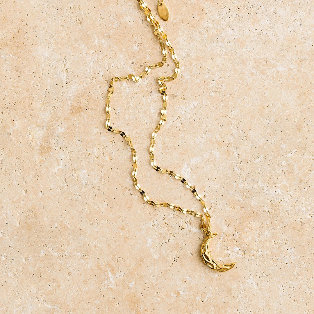 A gold chain necklace with a crescent moon pendant.