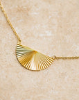 A thin gold necklace with a half sunburst pendant in the center.