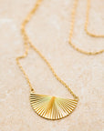 A thin gold necklace with a half sunburst pendant in the center.