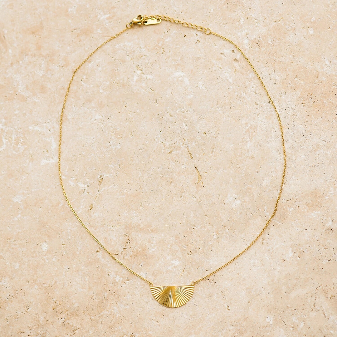 A thin gold necklace with a half sunburst pendant in the center.