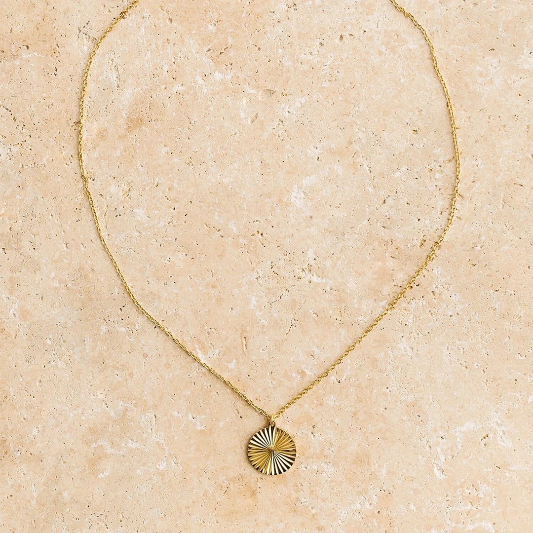 A dainty gold chain necklace with a round sun medallion pendant.