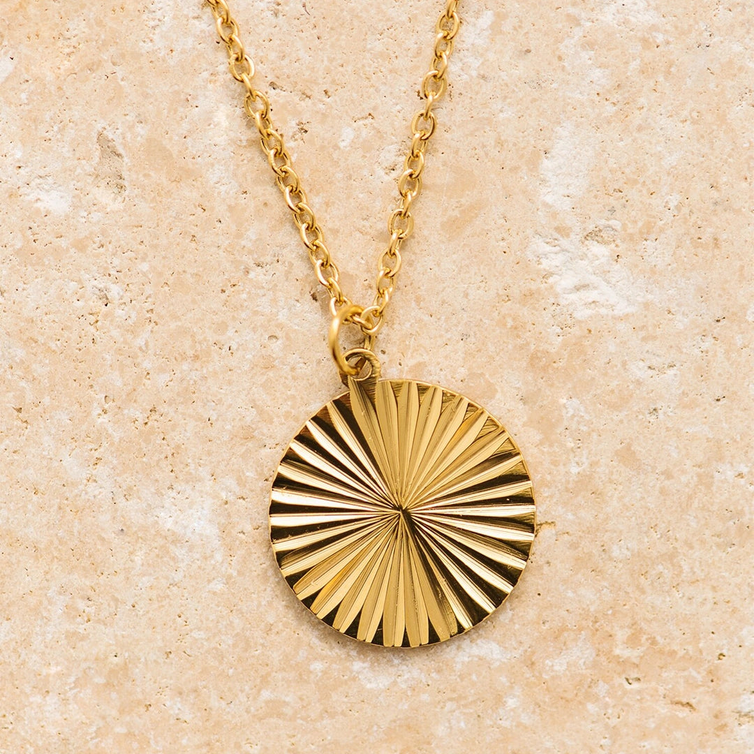 A dainty gold chain necklace with a round sun medallion pendant.