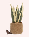 side view of a soft suede stuffed animal in the shape of a potted snake plant, with spikey dark and light green leaves, and brown textured pot with smiley face and dark brown floppy legs.