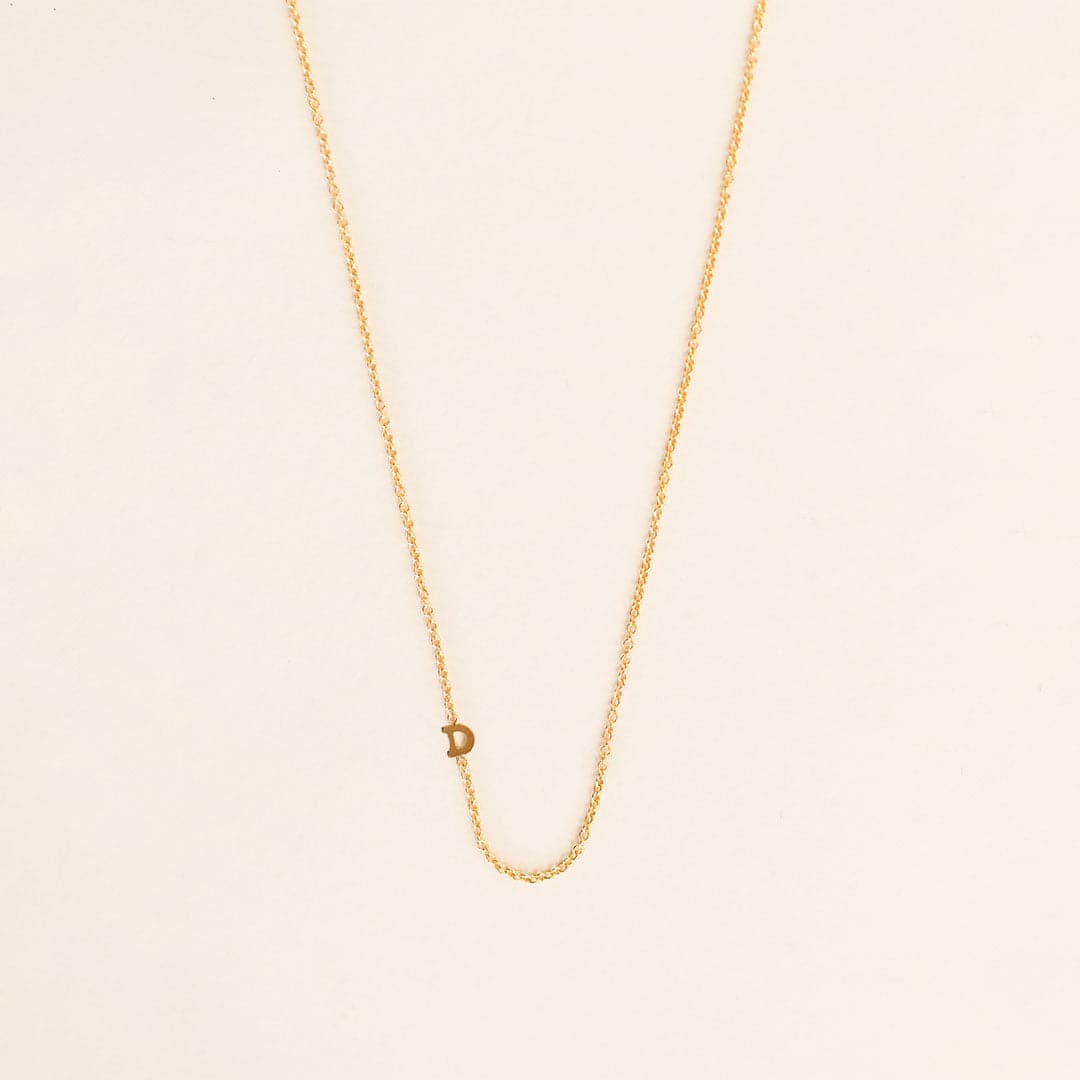 A dainty gold chain necklace with a tiny "D" secured within the chain. 
