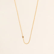 A dainty gold chain necklace with a tiny "D" secured within the chain. 