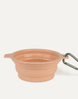 A peach silicone water bowl for pets that flattens when not in use. It also comes with a clip for attaching to your bag or leash on the go.