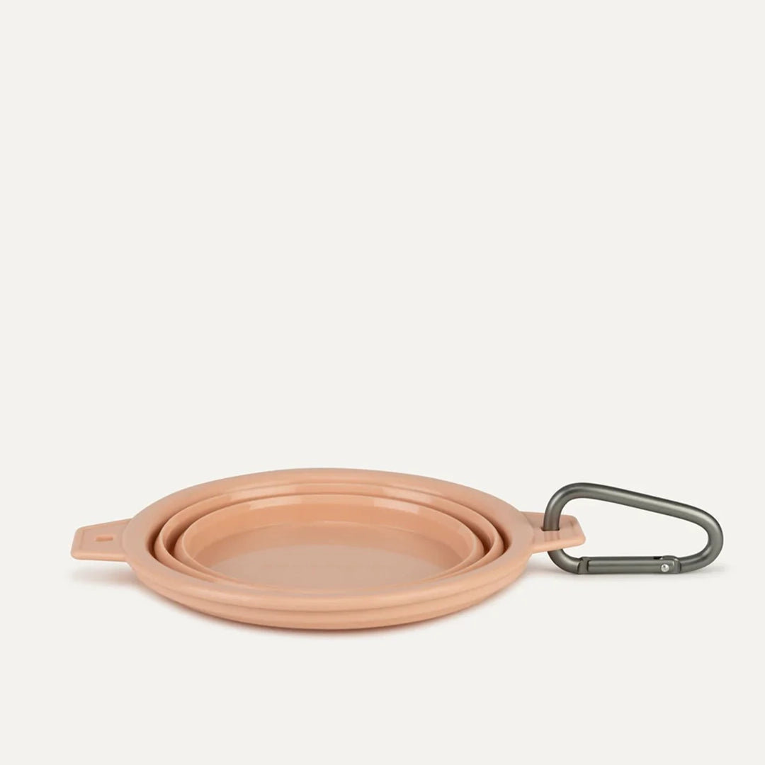 A peach silicone water bowl for pets that flattens when not in use. It also comes with a clip for attaching to your bag or leash on the go.