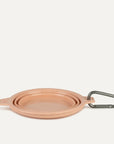 A peach silicone water bowl for pets that flattens when not in use. It also comes with a clip for attaching to your bag or leash on the go.