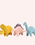 Photo of three felt dinosaur stuffed animals on a white surface. Left to right: yellow triceratops, pink stegosaurus with purple spikes, aqua brontosaurus.