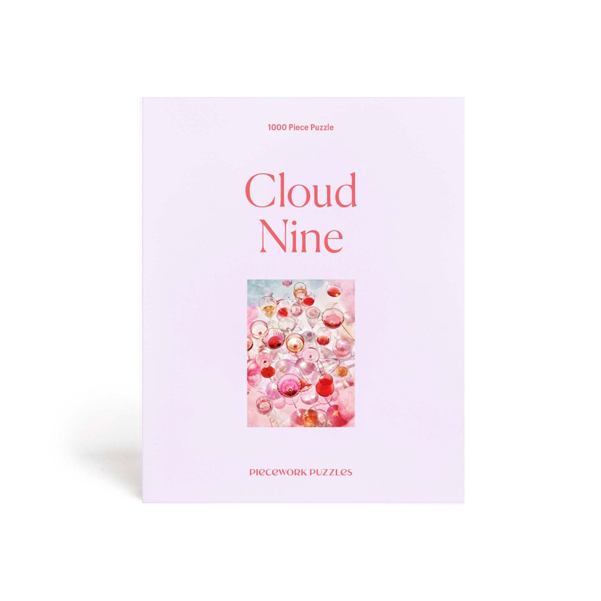 A lavender colored puzzle box that reads, &quot;Cloud Nine&quot; with a photo of what the puzzle looks like. The completed puzzle is a photo of an assortment of drinking glasses filled with a pink drink.