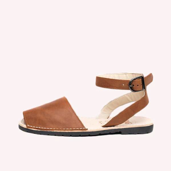  Single Avarca sandal made of lightweight dark rubber molded to a light natural leather sole. The sandal&#39;s front strap is a hazelnut brown and large enough to cover the front half of foot. Above is a thin leather ankle strap of the same color with a dark buckle closure. 