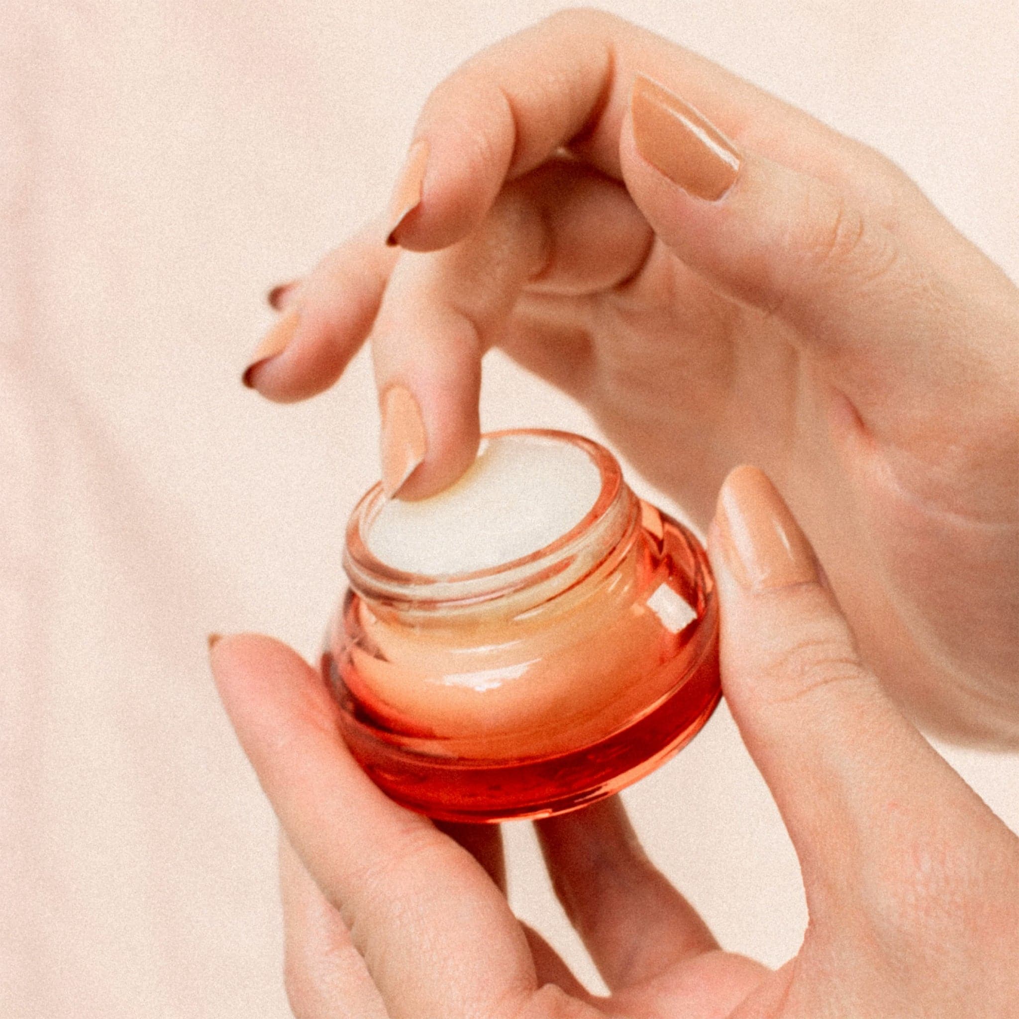 Someone using their finger to use this Lip scrub in a orange red container with a gold lid. This lip scrub is grainy, hydrating and perfect for your lips.