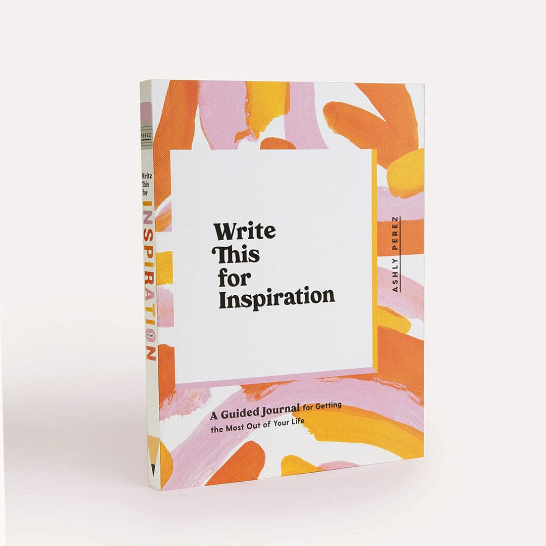 This journal is titled &#39;Write This for Inspiration by Ashly Perez&#39; in black lettering and has an enjoyable free-hand painted design with shades of pinks and oranges on top of a white background. The binding of the book is also white with the title spelt out in similar colorful lettering. 