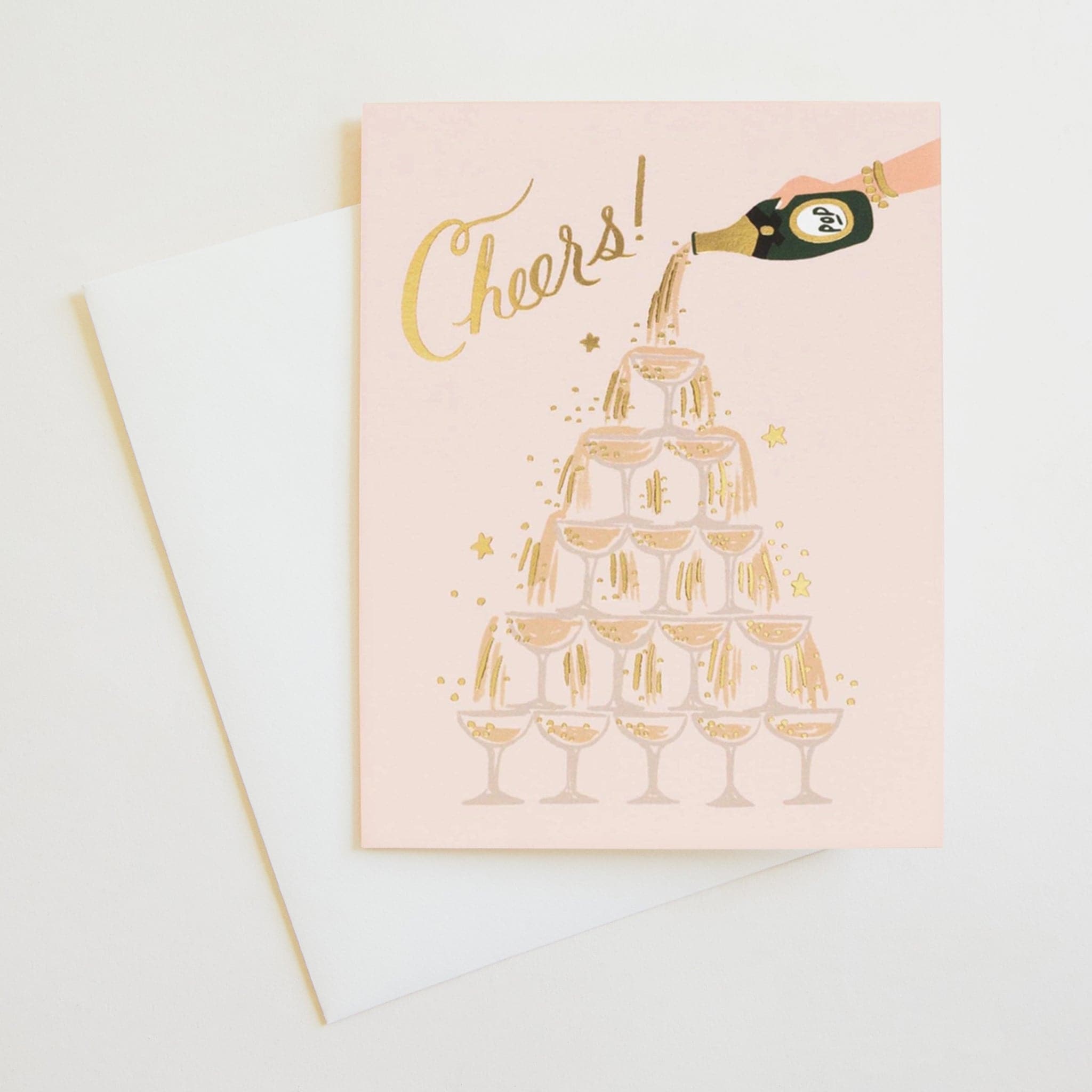 A celebration card! With Gold foil accents, this card features a champagne tower flowing with bubbly accented with gold foil. A hand is pouring champagne from the top, where it cascades all the way down. In gold foil cursive is written, "Cheers!". All of this is featured on a light pink background.