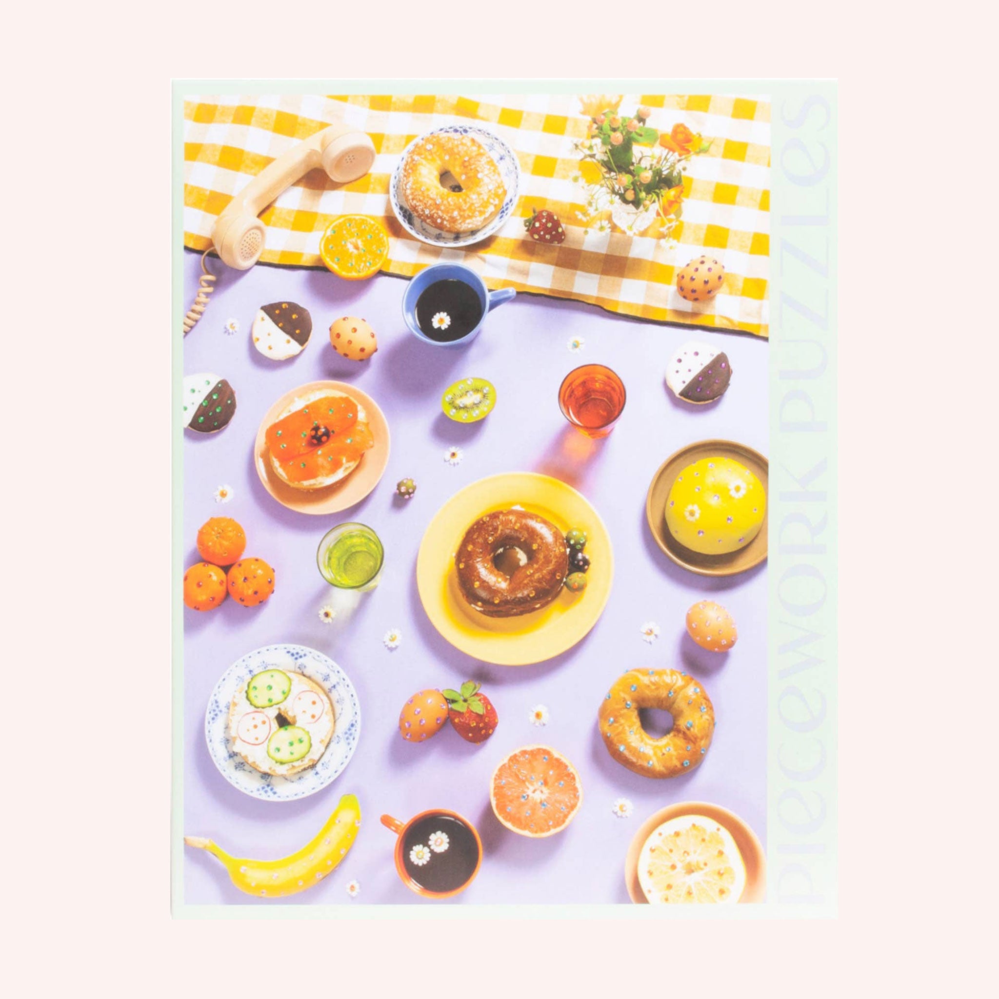 A look at what the completed puzzle looks like which is an array of bedazzled breakfast items including bagels, fruits, sunny side up eggs and more. The primary color tones of this puzzle include shades of light purple, yellow and orange.