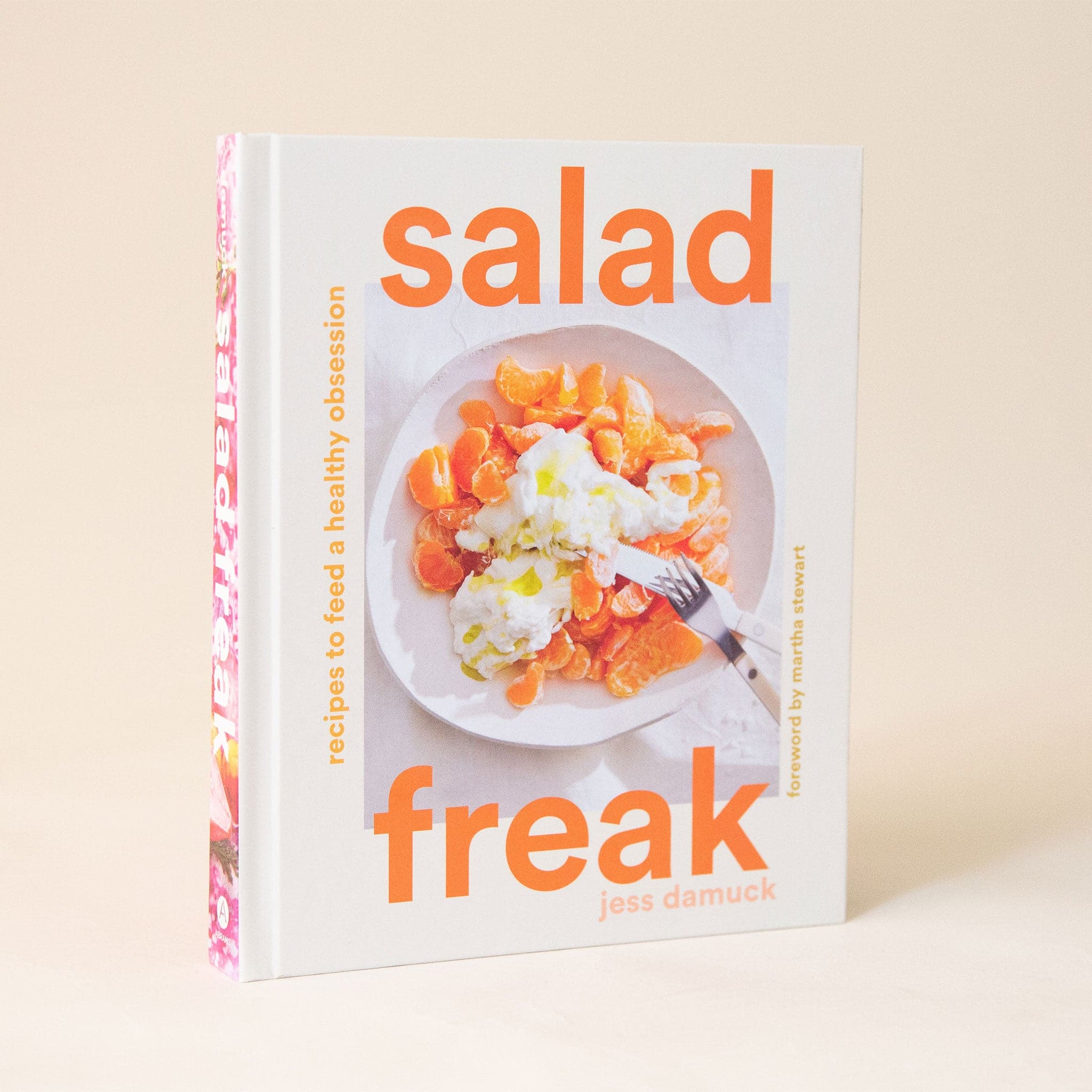 A white cookbook that has a bright orange text reading, &quot;Salad Freak, Recipies to feed a healthy obsession&quot;. The cover also has a photo of a vibrant Clemintine orange salad.