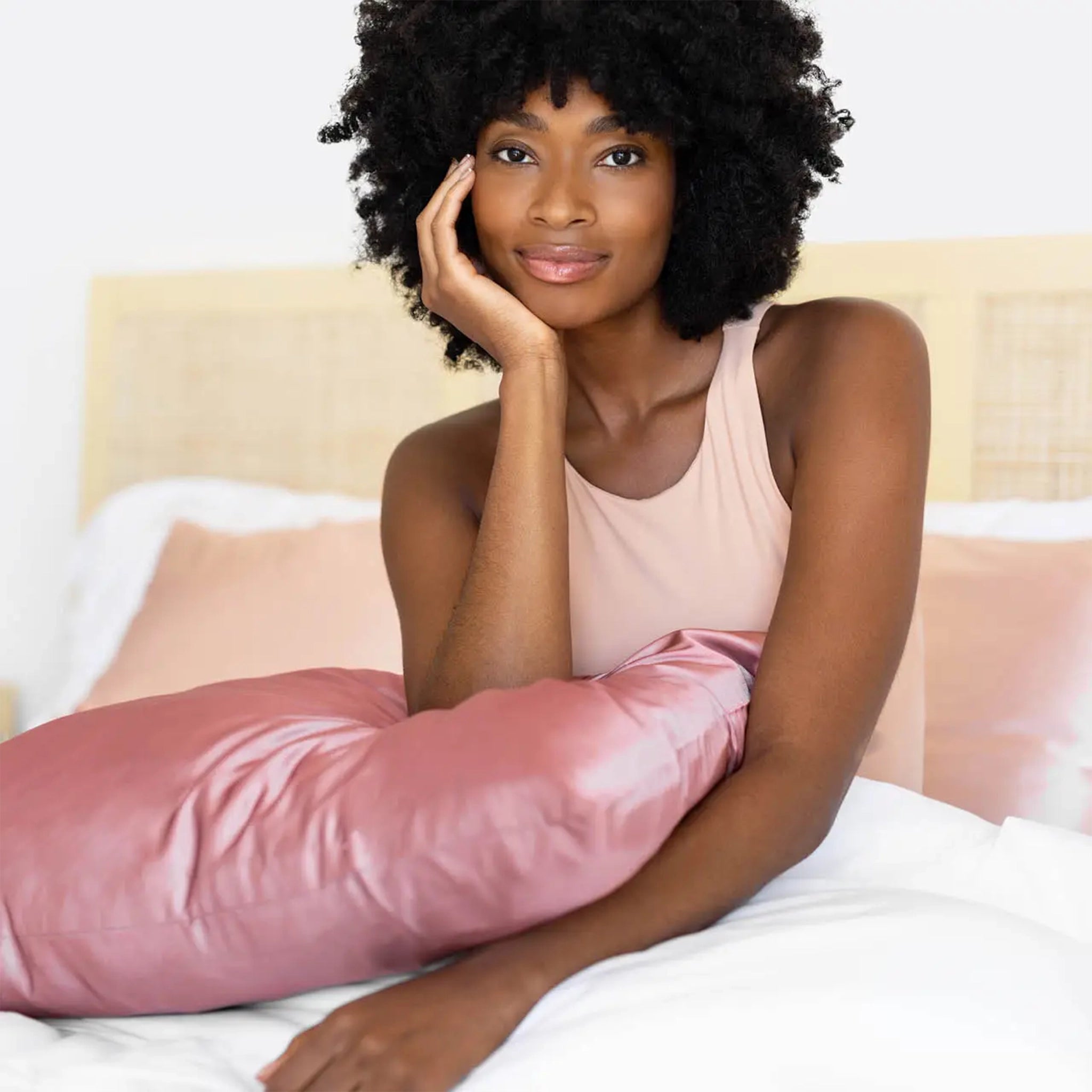 A rose pink satin pillow cover photographed with a model resting their elbow on it.