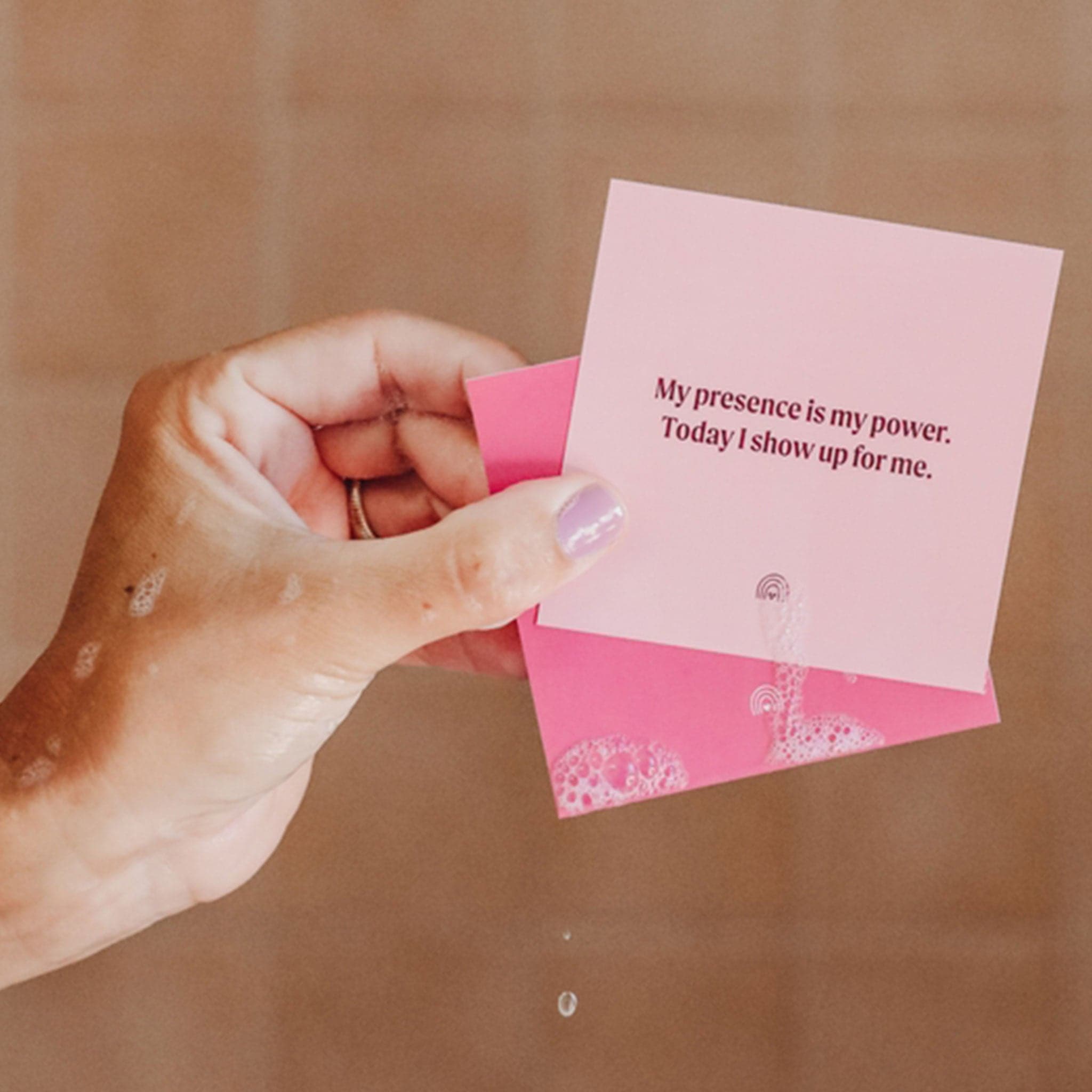 Different tones of pink cards that each have an uplifting affirmation on them for you to read and stick on the walls of your shower. This one pictured reads, &quot;My presence is my power. Today I show up for me.&quot;