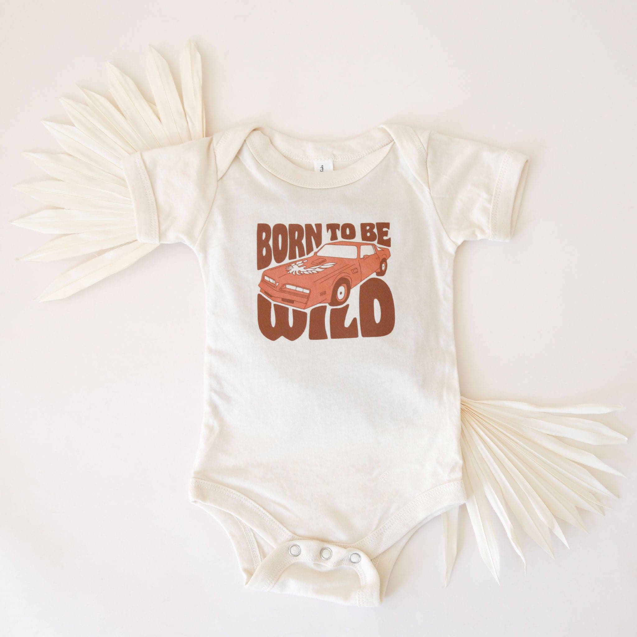 A white cotton onesie with a sports car and the text, &quot;Born To Be Wild&quot; in a brown groovy font.