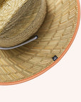 A wide brim sun set made of a neutral woven straw material with a white drawstring and tangerine orange detailing around the edge of the brim as well as the label in the center or the hat.