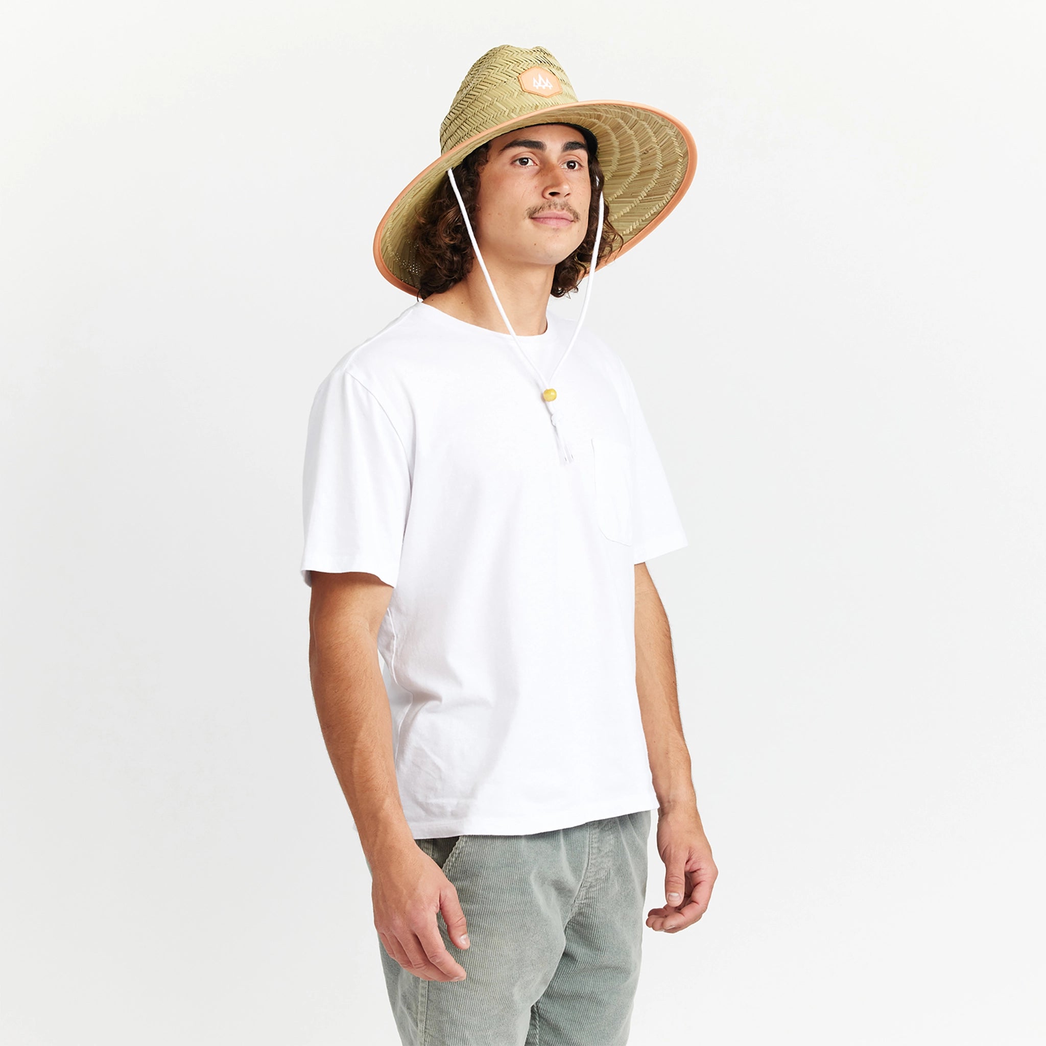 A wide brim sun set made of a neutral woven straw material with a white drawstring and tangerine orange detailing around the edge of the brim as well as the label in the center or the hat.