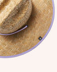 A woven straw sun set with a wide brim, a light purple drawstring and purple detailing underneath the brim of the hat as well as on the center label.