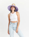 A woven straw sun set with a wide brim, a light purple drawstring and purple detailing underneath the brim of the hat as well as on the center label.