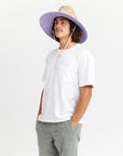 A woven straw sun set with a wide brim, a light purple drawstring and purple detailing underneath the brim of the hat as well as on the center label.