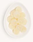 Birds eye view of a white egg shaped dish filled with light yellow candies. The candies are coated in white sugar.