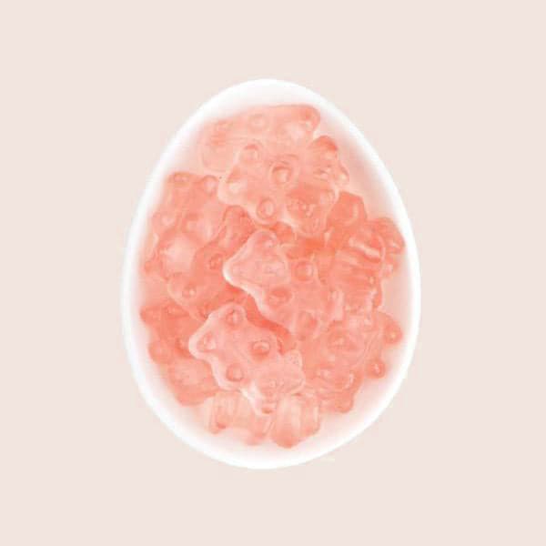 Birds eye view of a soft pink background with a white egg shaped dish in the middle. The dish is filled with light pink gummy bears.